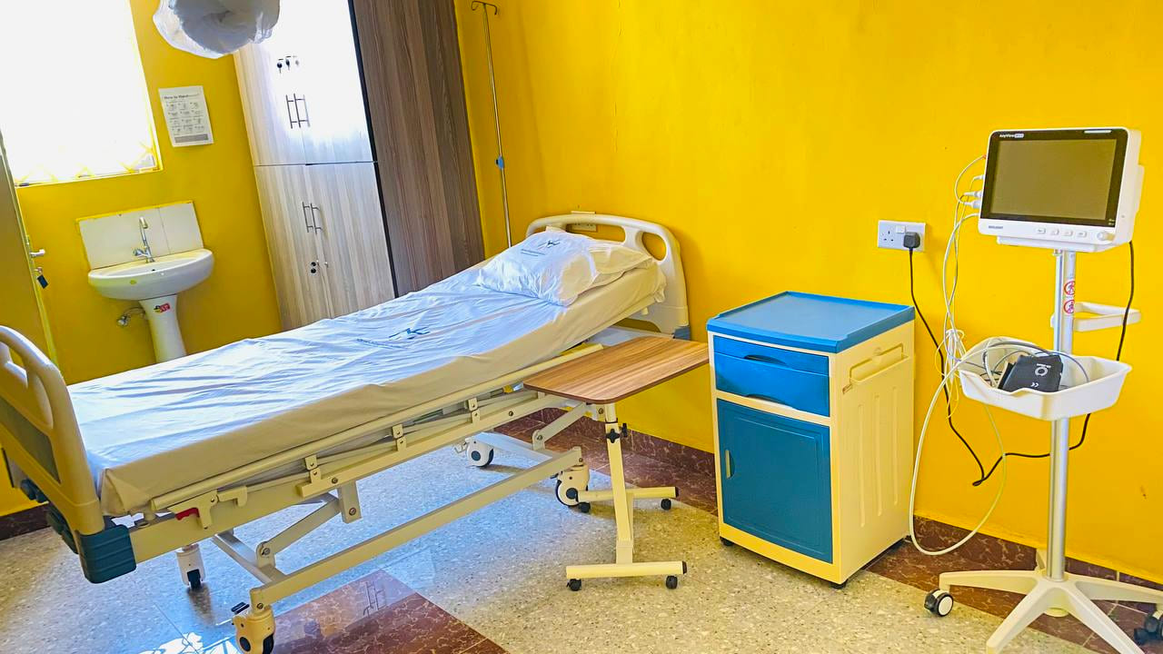 A private executive room at Namo Hospital, with an adjustable bed, an overbed table, a bedside cabinet, a patient monitor and an ensuite basin.